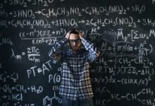 man in eyeglasses holding his head next to blackboard with math equations