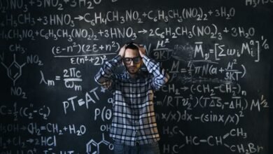 man in eyeglasses holding his head next to blackboard with math equations
