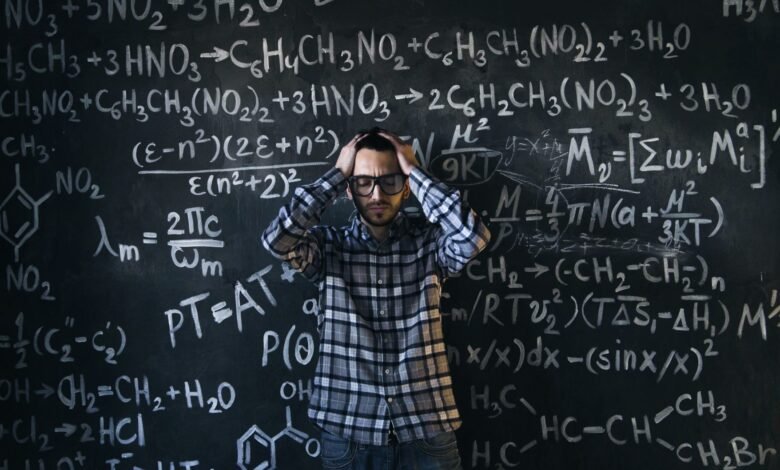 man in eyeglasses holding his head next to blackboard with math equations