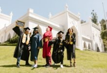 newly graduate students posing at the camera while standing on grass field