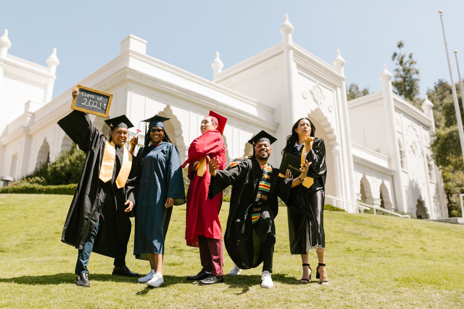newly graduate students posing at the camera while standing on grass field