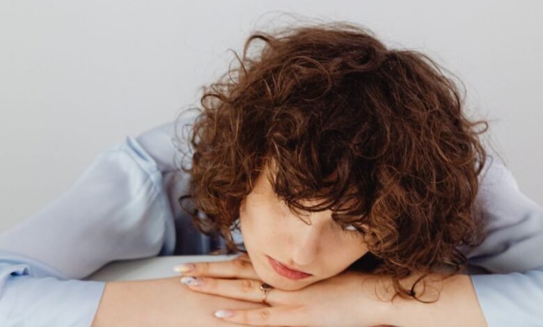a woman in blue long sleeves resting her head on the table with paper money while looking afar