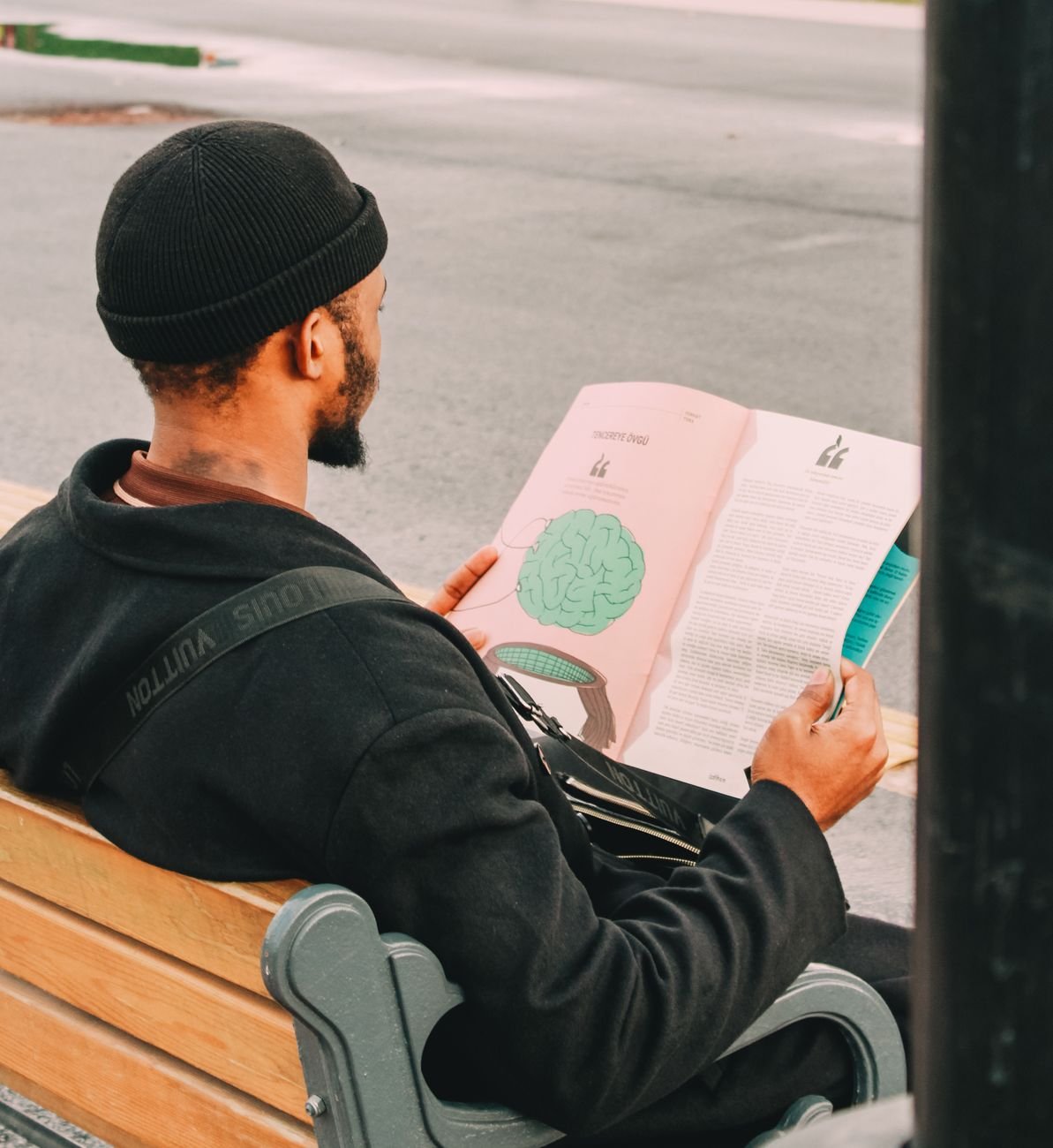 man reading magazine on park bench outdoors