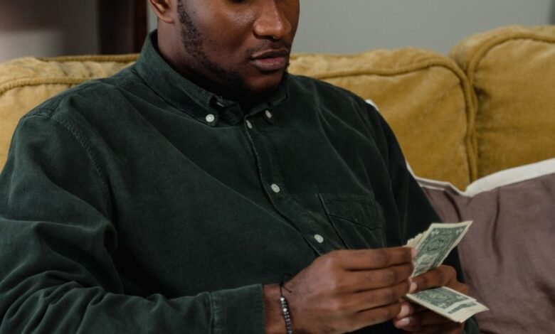 a man in black long sleeves counting his money while sitting on the couch