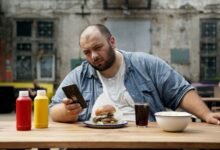 bald man sitting on wooden table looking at his smartphone