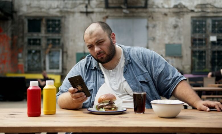bald man sitting on wooden table looking at his smartphone