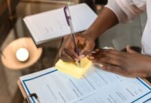 crop photo of woman writing on yellow sticky note pad