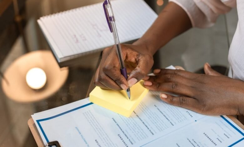 crop photo of woman writing on yellow sticky note pad