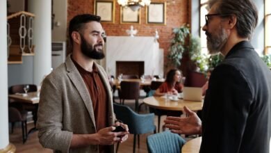 a man in black suit jacket talking to a man in brown suit jacket
