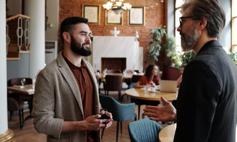 a man in black suit jacket talking to a man in brown suit jacket