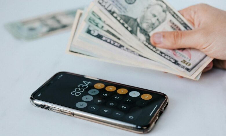 crop faceless person with cash and calculator app on smartphone