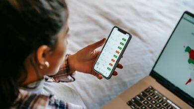 crop ethnic analyst using trading application on smartphone on bed