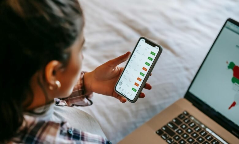 crop ethnic analyst using trading application on smartphone on bed