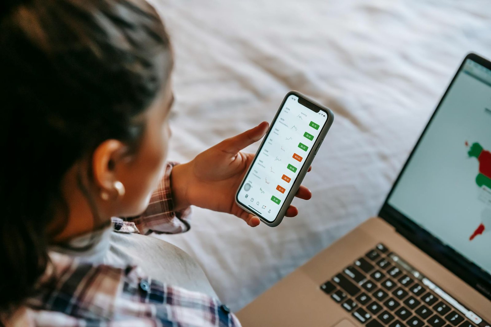crop ethnic analyst using trading application on smartphone on bed