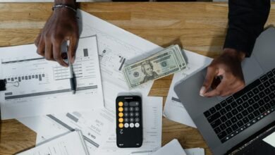 cash computer laptop pen and paperwork on wooden surface
