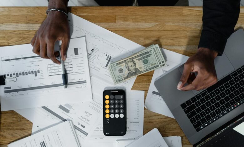 cash computer laptop pen and paperwork on wooden surface