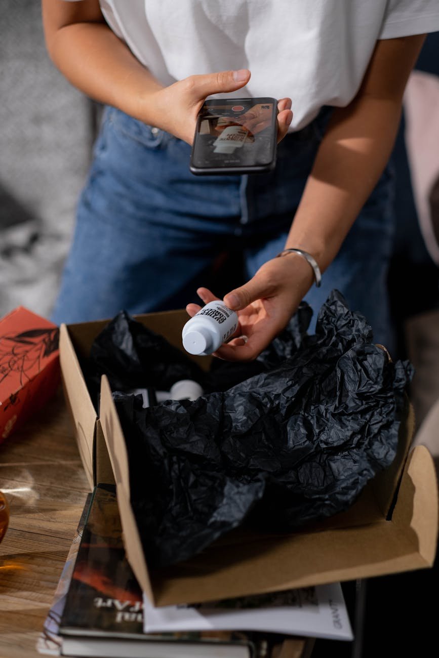 woman taking out a bottle out of a parcel and taking photo with her smartphone
