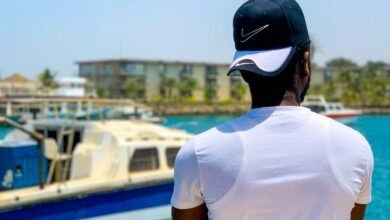 man in white shirt and blue cap standing near body of water