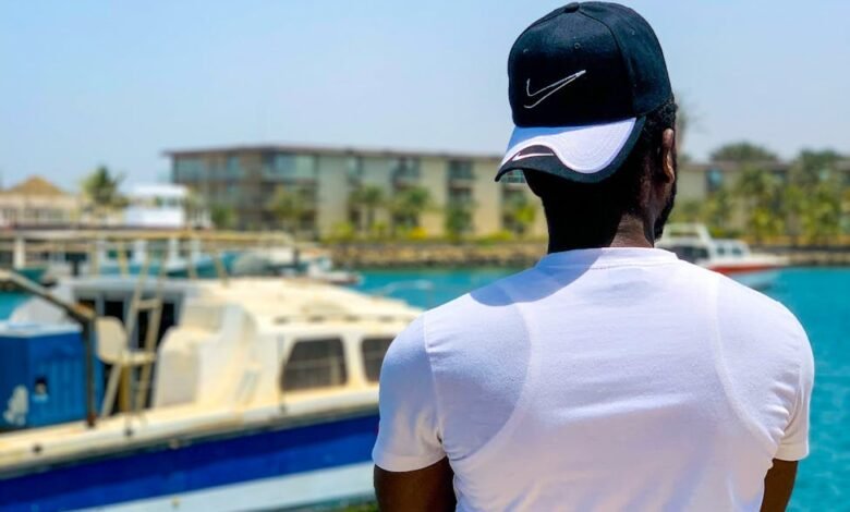 man in white shirt and blue cap standing near body of water
