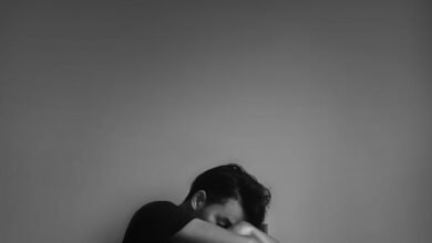 grayscale photography of man sitting beside wall