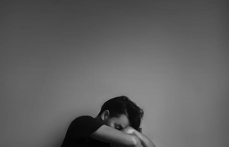 grayscale photography of man sitting beside wall