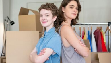 a woman in blue button up shirt standing beside a woman in gray tank top