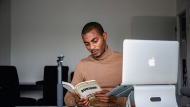man sitting and reading book near laptop