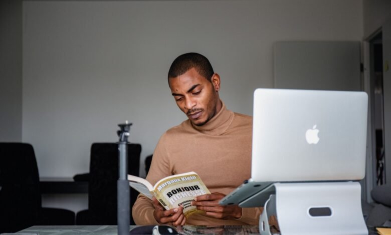 man sitting and reading book near laptop