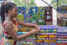 young woman standing next to piles of colorful patterned fabric