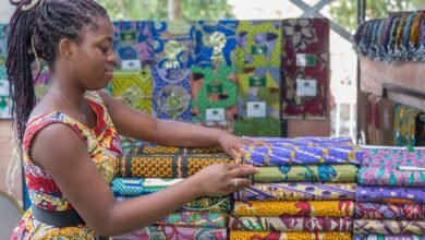 young woman standing next to piles of colorful patterned fabric