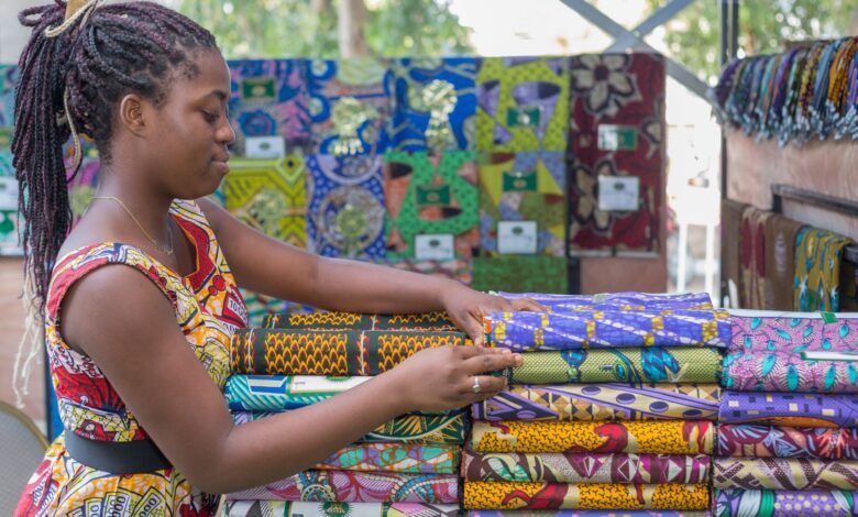 young woman standing next to piles of colorful patterned fabric