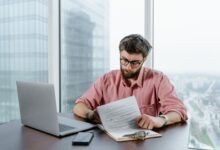 a man in pink long sleeves wearing eyeglasses while looking at the papers on the table
