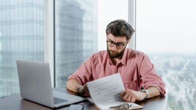a man in pink long sleeves wearing eyeglasses while looking at the papers on the table