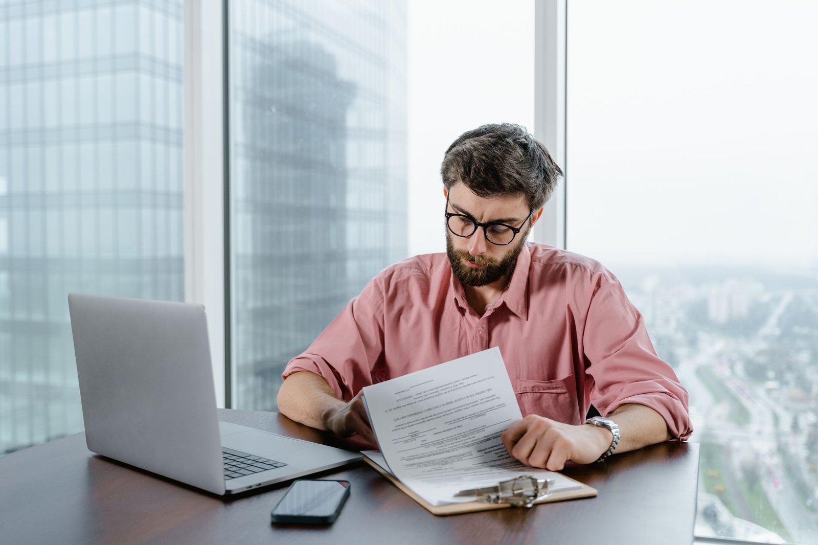 a man in pink long sleeves wearing eyeglasses while looking at the papers on the table